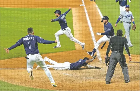  ?? PHOTOS BY ERIC GAY/ASSOCIATED PRESS ?? Rays players celebrate as Randy Arozarena, on the ground on home plate, scores the winning run in the ninth inning of Game 4 of the World Series on Saturday in Arlington, Texas. The Rays evened the series at 2-2.