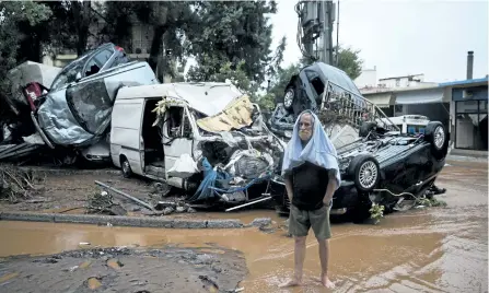 ?? PETROS GIANNAKOUR­IS/ THE ASSOCIATED PRESS ?? A barefoot man stands in front of a pile of vehicles in the municipali­ty of Madra western Athens, on Wednesday. Flash floods in the Greek capital’s western outskirts turned roads into raging torrents of mud and debris, killing at least 14 people,...