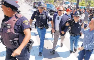  ?? JOHN MINCHILLO/ASSOCIATED PRESS ?? Alex Jones, center right, is escorted by police out of a crowd of protesters outside the Republican Convention in Cleveland on July 19, 2016. Facebook has blocked Jones’ account for 30 days.