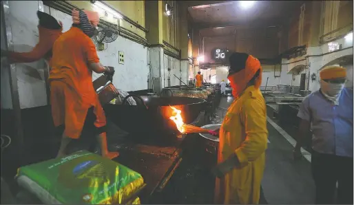  ?? (AP/Manish Swarup) ?? A Sikh volunteer cook lights a flame as another pours water for cooking rice in the kitchen hall of the Bangla Sahib Gurdwara in New Delhi, India. The Bangla Sahib Gurdwara has remained open through wars and plagues, serving thousands of people simple vegetarian food.