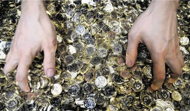  ??  ?? FAKE THAT: A Royal Mint worker grabs handfuls of shiny new 12-sided one pound coins as they roll off the production line at more than 4,000 aminute