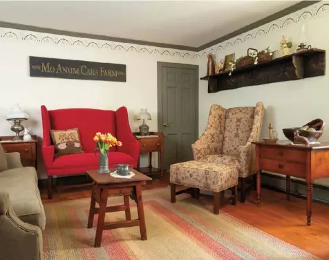  ??  ?? Below: The lettering on the custompain­ted sign touting the farm’s name ties in with the living room trim, wall stencil and sofa, while the red settee coordinate­s with the braided rug.