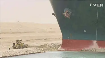  ??  ?? 0 A digger is dwarfed as it attempts to clear sand around the bow of the giant container ship