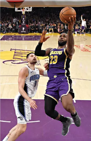  ?? AP Photo/Mark J. Terrill, File ?? ■ Los Angeles Lakers forward LeBron James, right, shoots as Orlando Magic center Nikola Vucevic defends during the second half Jan. 15 in Los Angeles. The Milwaukee Bucks and the Lakers already have just about guaranteed themselves the top two playoff seeds and face a delicate balancing act when the NBA returns to action. They must try to shake off the rust after a 4 1/2-month hiatus while also staying as healthy as possible for the postseason.