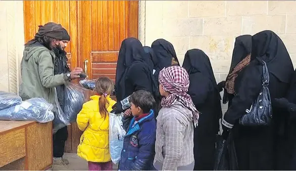  ?? MILITANT WEBSITE VIA THE ASSOCIATED PRESS ?? Members of the Islamic State group, left, distribute niqabs, enveloping black robes and veils that leave only the eyes visible, to Iraqi women in Mosul, northern Iraq. Even after leaving areas controlled by Islamic State, some women chose to continue to wear the niqab. “Allah gave the niqab to the women,” said one woman.