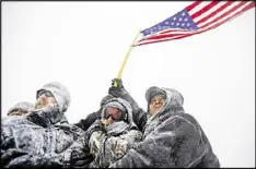  ?? DAVID GOLDMAN / AP ?? Military veterans huddle together to hold a United States flag against strong winds during a march to a closed bridge outside the Oceti Sakowin camp where people have gathered to protest the Dakota Access oil pipeline in Cannon Ball, N.D., Monday.