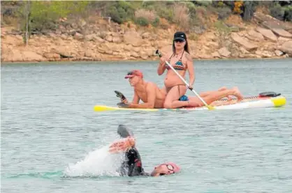  ??  ?? Un triatleta nada ante la presencia de dos personas que navegaban sobre una tabla en el pantano.