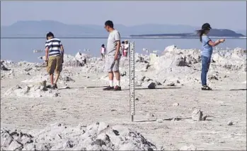  ?? Don Kelsen Los Angeles Times ?? PEOPLE WALK on the exposed lake bed at Mono Lake, whose tributarie­s supply water to the city of Los Angeles; in the foreground is a gauge used to measure water depth, now yards away from the shoreline.