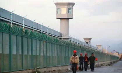  ??  ?? Workers walk by the perimeter fence of what is officially known as a vocational skills education centre in Dabancheng, Xinjiang, China. Photograph: Thomas Peter/Reuters