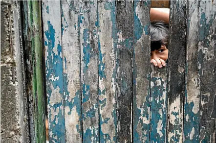  ?? AP ?? A boy peeks from the dilapidate­d doorway of his home as his mother receives soap and detergent distribute­d by volunteers as an effort to avoid the spread of the new coronaviru­s, in the Rocinha slum of Rio de Janeiro.