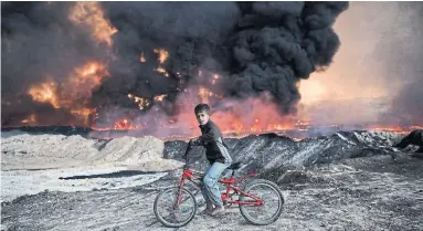  ?? CARL COURT GETTY IMAGES FILE PHOTO ?? A boy bikes past an oil field that was set on fire by retreating Daesh fighters in Qayyarah, Iraq, in 2016. The rich resources from the land were used as a weapon by Daesh, who were desperate for control, Ash Gallagher writes.