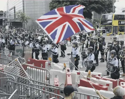  ??  ?? A man waves a British flag as policemen in anti-riot gear stand guard against the protesters in Hong Kong