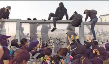  ?? Miguel Candela EPA/Shuttersto­ck ?? PRO-DEMOCRACY marchers scale a wall in Hong Kong’s Tsim Sha Tsui district. Earlier Sunday, some demonstrat­ors called for President Trump to “make Hong Kong great again” and for police to stop using tear gas.