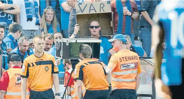  ?? PHOTONEWS / GETTY ?? Un colegiado revisa el monitor de campo durante el playoff de la Liga belga ante un espectador que se mofa del videoarbit­raje