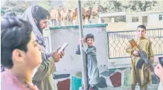  ??  ?? A boy poses for a picture with the rifle of a Taliban fighter near the camel enclosure at the Kabul zoo