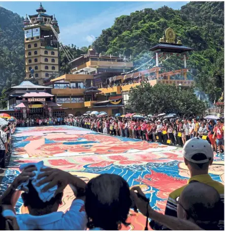  ?? — AFP ?? Marking the occasion: Devotees unfurling a 25-year-old, 196-foot-long sacred ‘thangka’ at the Enlightene­d Heart Tibetan Buddhist Temple in Ipoh. The thangka is a painting on cotton or silk clothing which usually depicts a deity of Buddhism in a scene or a mandala.