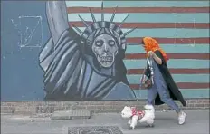 ?? Vahid Salem/Associated Press ?? A woman walks her dog past an anti-U.S. mural painted on the wall of the former U.S. Embassy on Tuesday in Tehran,
