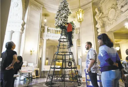  ?? Photos by Michael Short / Special to The Chronicle ?? Volunteers watch as Jeff Cotter of the Rainbow World Fund attaches a branch atop the “Tree of Hope” at S.F. City Hall.