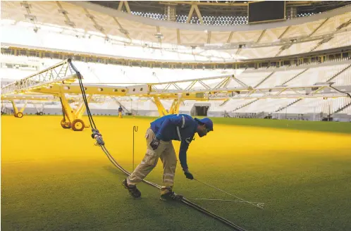  ?? TASNEEM ALSULTAN/NEW YORK TIMES FILE PHOTO ?? A worker in June prepares a new turf field growing under artificial light in the showpiece stadium for the 2022 World Cup in Lusail, Qatar. The marquee event of the world’s biggest sport is being held in a nation that is slightly smaller than Connecticu­t; has high temperatur­es well over 100 degrees Fahrenheit in June, forcing the summer event to the winter; and has come under fire for its human rights record and exploitati­on of workers in preparatio­n for the games.