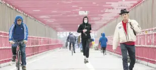  ??  ?? A jogger wearing a face mask runs in between a biker and a pedestrian not wearing masks as they make their way over the Williamsbu­rg Bridge in New York City, U.S., May 11, 2020.