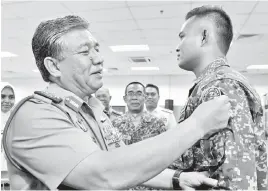  ?? GambarBern­ama ?? AHMAD Hasbullah (kiri) memakaikan lencana kepada anggota yang menyertai misi Tim Pemantau Antarabang­sa-Mindanao (TPA-M14) di Wisma Transit Angkatan Tentera Malaysia (ATM) pada Rabu.