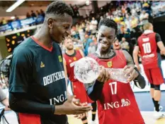  ?? Foto: Axel Heimken, dpa ?? Dennis Schröder (rechts) und Isaac Bonga halten den Pokal nach dem Sieg im dritten Spiel in den Händen.