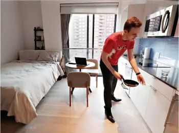  ?? AP Photo/Kathy Willens ?? ■ Carmel Place resident Matthew Alexander puts away dishes in his studio apartment May 1 in the Kips Bay neighborho­od of Manhattan in New York. After sharing space with roommates, Alexander moved into a co-living space building, where he likes the minimalist living style. Although the apartment is small, the building provides multiple amenities, including weekly housekeepi­ng, grocery delivery and dry cleaning pickup, plus a gym and a rooftop terrace.