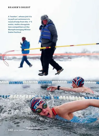  ??  ?? A ‘hooker’, whose job it is to pull out swimmers in need of help from the -1°C water, walks alongside two competitor­s at the Memphremag­og Winter Swim Festival