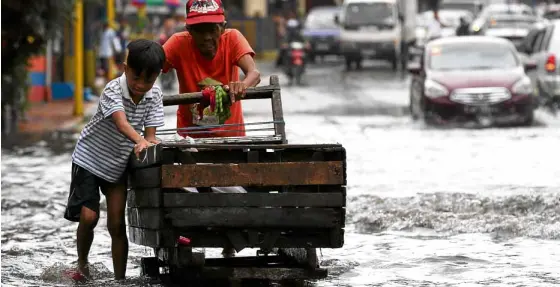 ?? LYN RILLON ?? TOUGH TERRAIN A boy takes a break from playtime in the flood to help an elderly man push his cart through an inundated area on Nueve de Febrero Street in Mandaluyon­g City.—