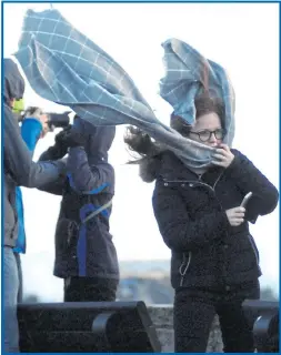  ??  ?? Two brave the sea spray crashing on the pier at West Bay, Dorset, yesterday as, right, a girl battles with her scarf while holding her phone in the high winds