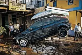  ?? ARGIRIS MADIKOS/EUROKINISS­I ?? Business hangs in the balance: A store worker cleans up damage Tuesday in front of a washed-up and oddly suspended vehicle following a storm on the Greek island of Symi.