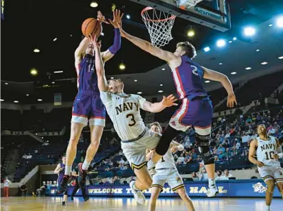  ?? TERRANCE WILLIAMS/FOR CAPITAL GAZETTE ?? American forward Johnny O’Neil, left, blocks a shot by Navy guard Sean Yoder during the second half of Thursday night’s Patriot League Tournament quarterfin­al at Alumni Hall.