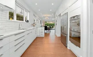  ??  ?? The well-designed kitchen boasts timber floors, sleek white cabinetry, Corian benchtops and a spacious scullery.