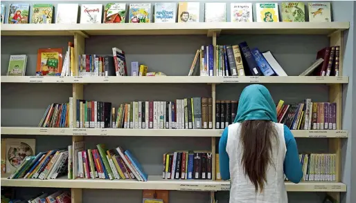  ?? AFP ?? A woman refugee looks at a book shelf at a library set up on the premises of an internatio­nal non-government­al organisati­on hosting Syrian and Afghan women and children, in central Athens. There are increasing initiative­s in Greece to offer reading and...