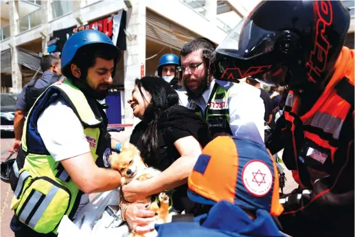  ?? (Amir Cohen/Reuters) ?? A WOMAN holding her dog is evacuated by medics after a rocket launched from the Gaza Strip hit a shopping complex in Ashkelon on Tuesday.