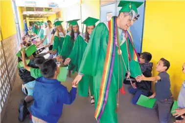  ?? MARLA BROSE/JOURNAL ?? Albuquerqu­e High graduating senior Aidan Martinez, front, high fives a class of students, including Craig Janis, bottom right, who line the halls of East San Jose Elementary on Friday. The school’s students cheered on a group of graduates as they...