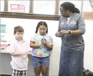  ?? Brodie Johnson • Times-Herald ?? The Forrest City Public Library’s summer reading program today featured an activity with Marla Lane, the EFNEP program assistant for the St. Francis County SFC Extension Service, where children learned the most effective hand washing technique. Lane, right, is joined by two children as one cleans their hands with hand sanitizer while the other uses an alcohol wipe. Another child, not pictured, washed their hands with soap and water.