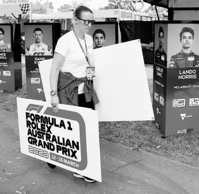  ?? AP ?? A woman takes away signs after the cancellati­on of the Australian Formula One Grand Prix in Melbourne, yesterday.