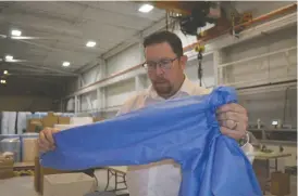  ??  ?? David Glover, who co-owns Harbour with his brother, Andrew Glover, inspects an
isolation gown made in the company’s Windsor, ON facility.