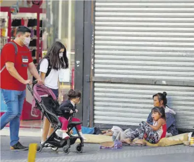  ?? AGUSTÍN MARCARIAN / REUTERS ?? Una mujer pide dinero en la calle con sus hijos mientras una familia pasea, en Buenos Aires.