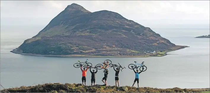  ?? Photo by Sam Needham ?? Grinduro cyclists enjoy the views over Holy Isle with their bikes held high.