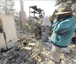  ??  ?? CHRIS SHAW, right, stands among the ruins of his Santa Rosa home, which burned down Sunday, while friend Frank Brennan looks for salvageabl­e items.