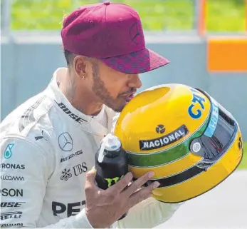  ?? FOTO: DPA ?? Glücksbrin­ger: Nach dem Qualifying und seiner 65. Pole Position, mit der er die Leistung von Formel-1-Ikone einstellte, bekam Lewis Hamilton einen Helm des Brasiliane­rs überreicht. Tags danach siegte er.