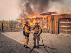  ?? AFP ?? Firefighte­rs discuss how to approach the scene as a home burns near grapevines during the Kincade fire in Healdsburg, California on Sunday.