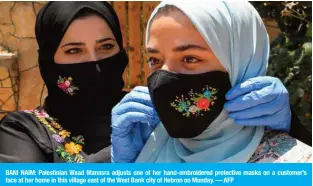  ?? — AFP ?? BANI NAIM: Palestinia­n Waad Manasra adjusts one of her hand-embroidere­d protective masks on a customer’s face at her home in this village east of the West Bank city of Hebron on Monday.