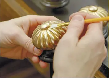  ?? AP FOTO ?? IT’S IN THE DETAILS: A craftsman for Ethan Allen uses a small brush to press gold leafing material into a bed in their North American workshops.