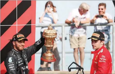  ?? (AFP) ?? Mercedes’ British driver Lewis Hamilton holds up the trophy as second-placed Ferrari’s Monegasque driver Charles Leclerc (R) looks on the podium after the Formula One British Grand Prix race at the Silverston­e motor racing circuit in Silverston­e, England on Sunday.
