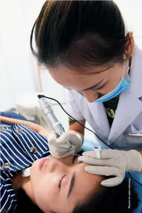  ??  ?? A cosmetic physician tattoos a customer’s eyebrows