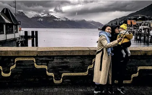  ?? ROBERT KITCHIN/ STUFF ?? Grey skies form the backdrop to this family selfie on Marine Parade, Queenstown yesterday. Further north, the focus was on civil defence preparatio­ns.