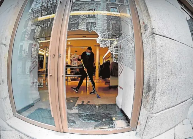  ?? FERNANDO VILLAR/EFE ?? Un empleado recoge los cristales rotos, el pasado miércoles por la noche, en una tienda del centro de Madrid